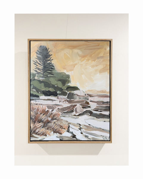A framed landscape painting featuring a dark green pine tree, rocky terrain, and a warm golden sky, with a Raw oak shadowbox frame
